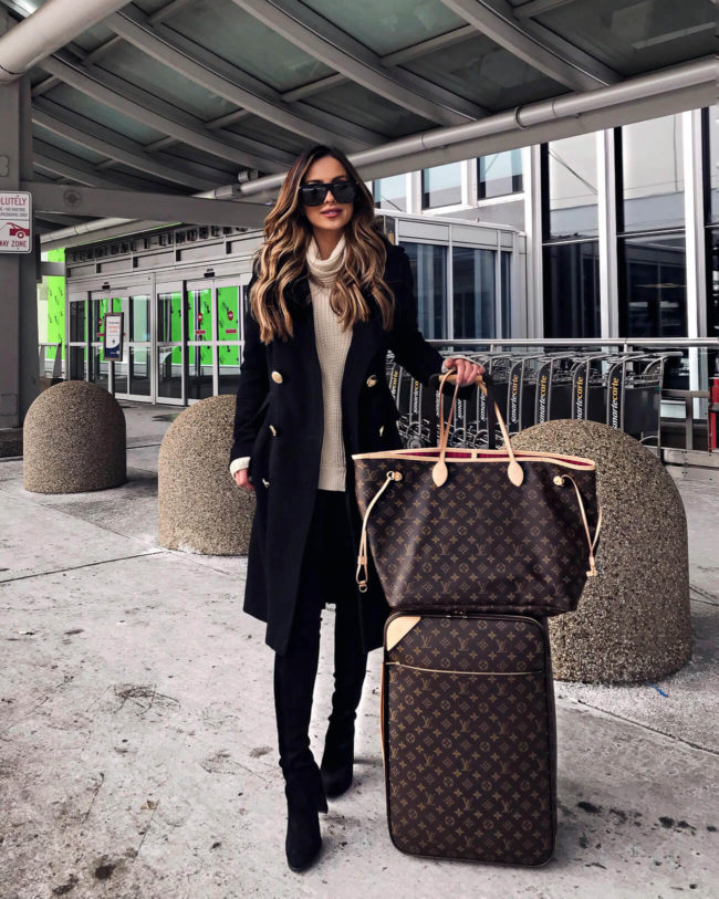 fashion blogger mia mia mine wearing a black coat and louis vuitton luggage to travel