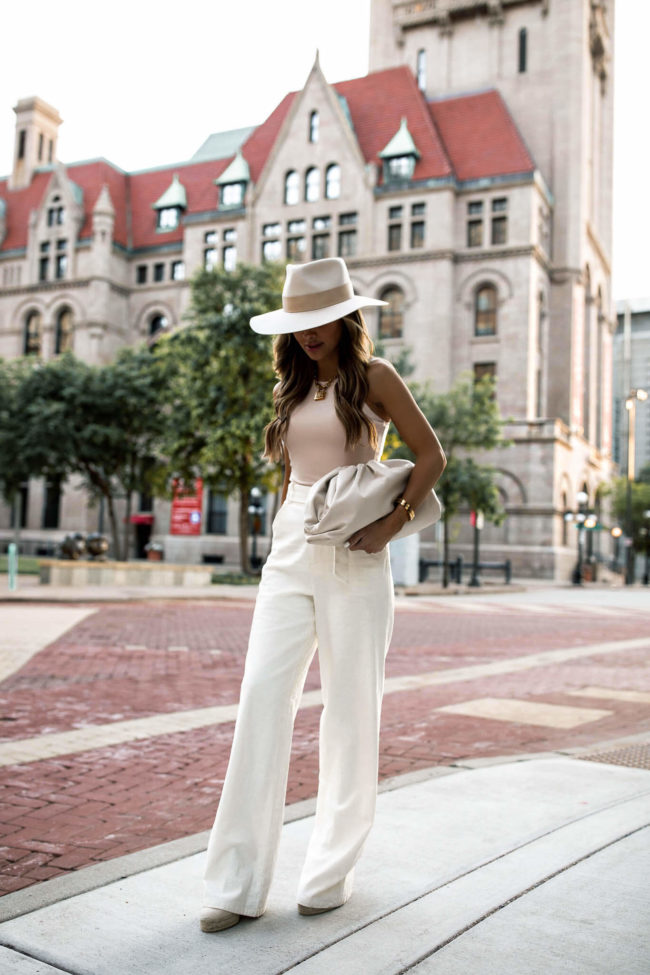 fashion blogger mia mia mine wearing white linen pants and a janessa leone hat while sharing bottega veneta the pouch bag review