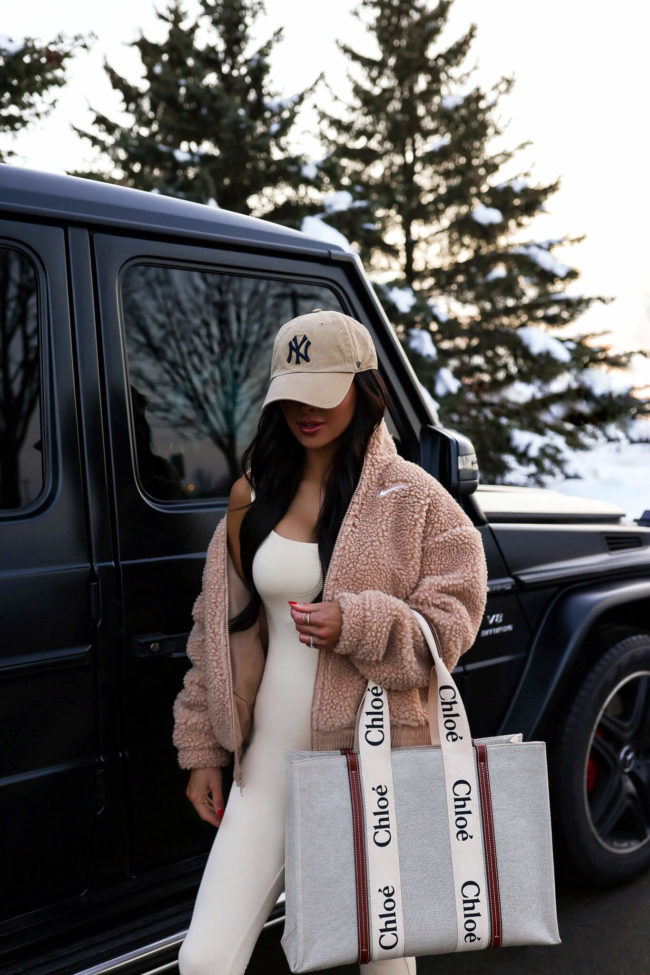 fashion blogger mia mia mine wearing a white jumpsuit and a nike sherpa jacket from nordstrom